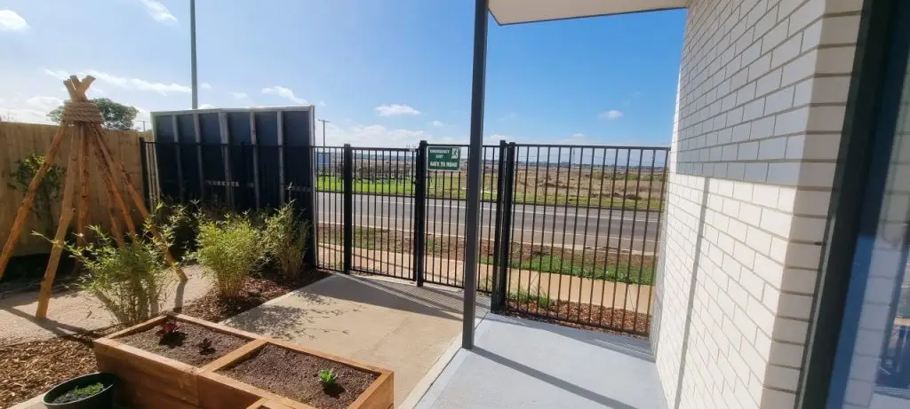 Black steel boundary fence and pedestrian gate beside a paved entrance