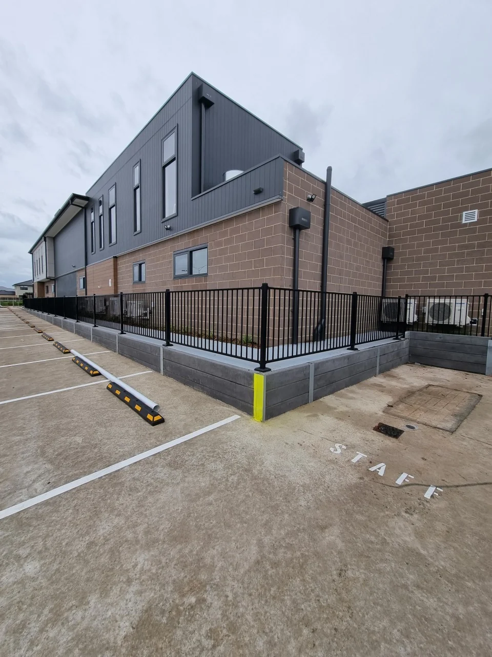 Concrete sleeper retaining wall and black tubular fence beside the Derrimut childcare car park
